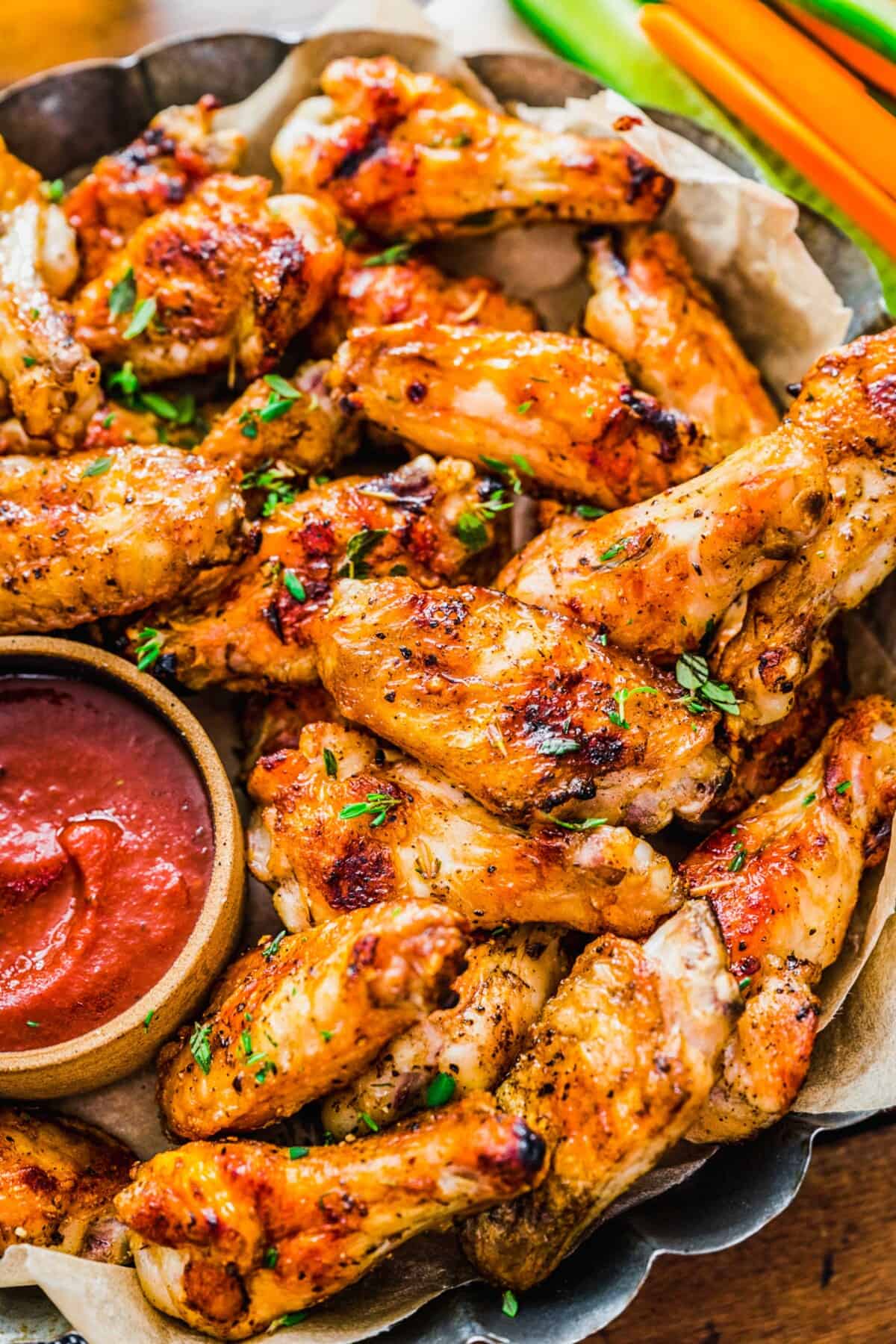 grilled chicken wings next to a red sauce and sliced cucumbers and carrots