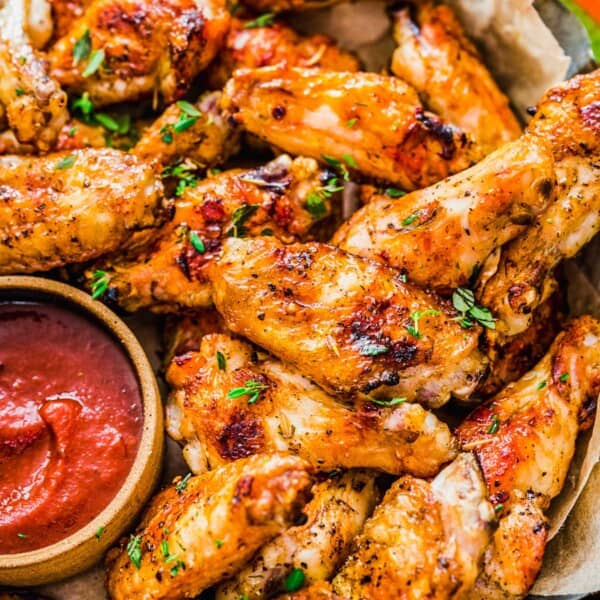 grilled chicken wings next to a red sauce and sliced cucumbers and carrots