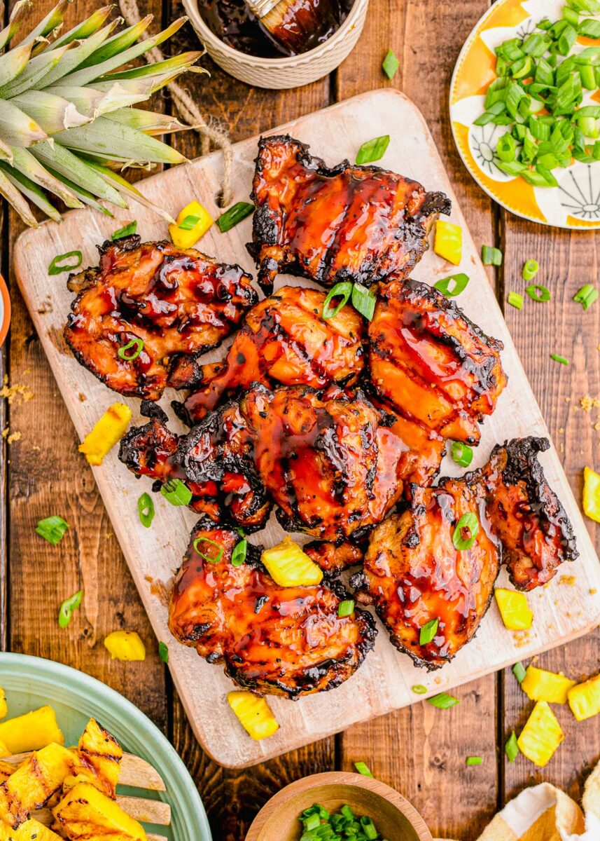 Grilled and glazed chicken thighs are placed on a wooden cutting board. 