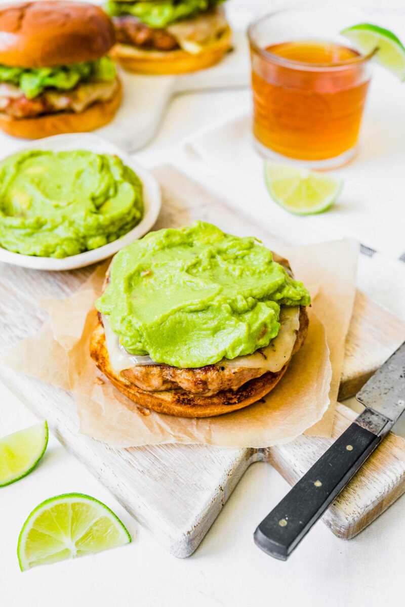Avocado is smeared across the top of a cheesy burger patty. 