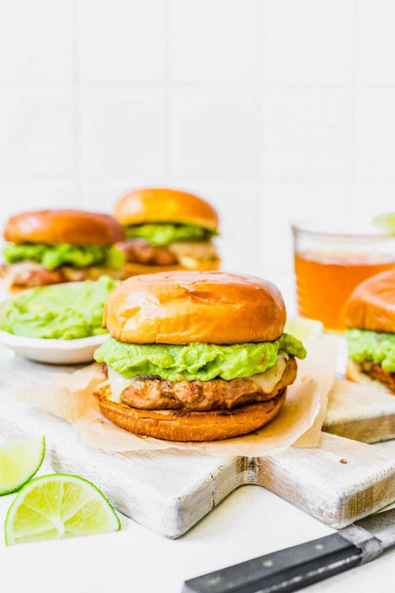 A turkey and chorizo burger with avocado is placed on a wooden cutting board. 