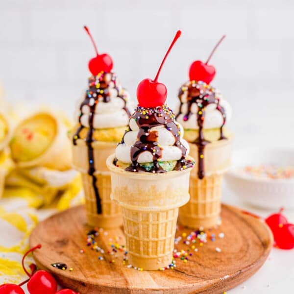 Three ice cream cone cupcakes are placed on a wooden serving plate.