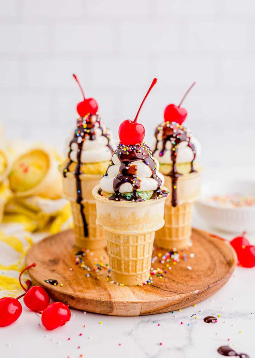 Three ice cream cone cupcakes are placed on a wooden serving plate. 
