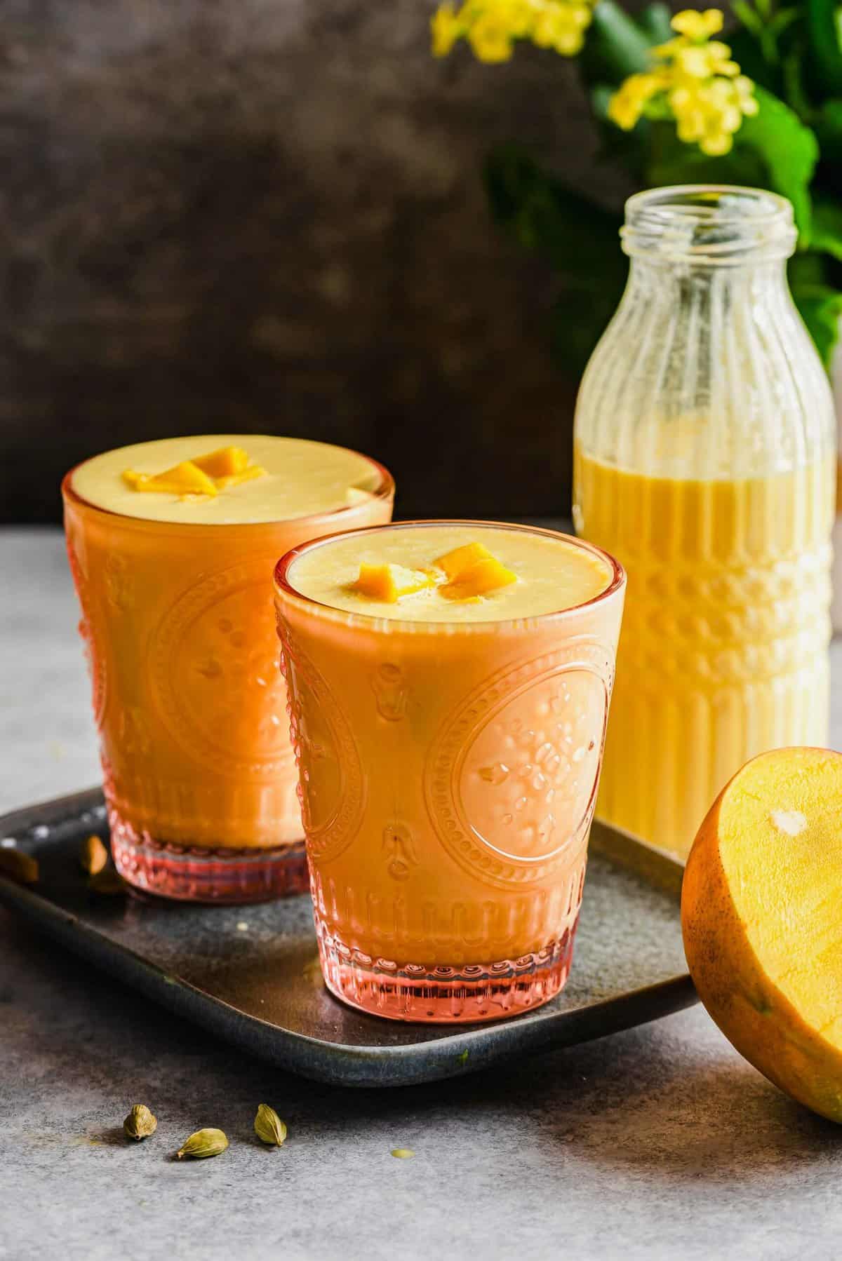 Tray with two glasses of mango lassi, with bottle in background