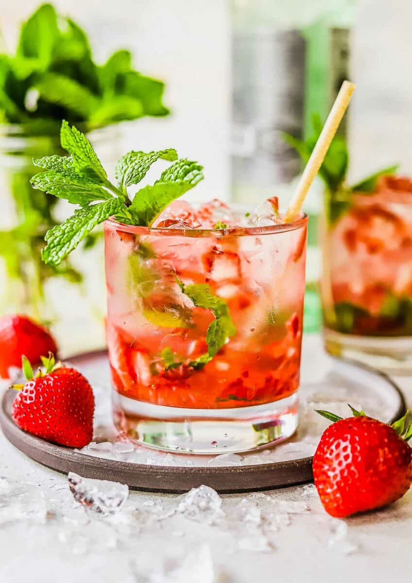 A strawberry mojito in a short cocktail glass is garnished with a mint sprig. 