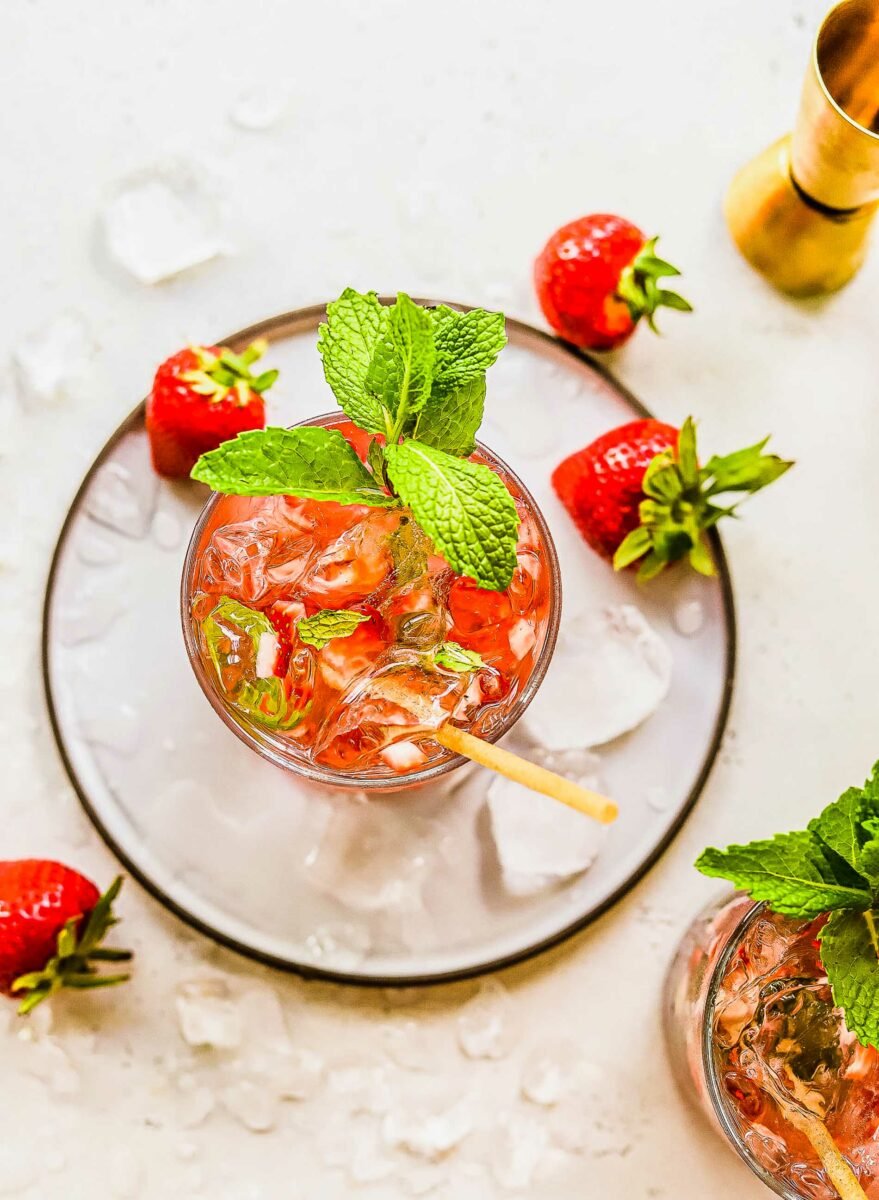 A wooden stirrer is placed in a garnished strawberry mojito. 