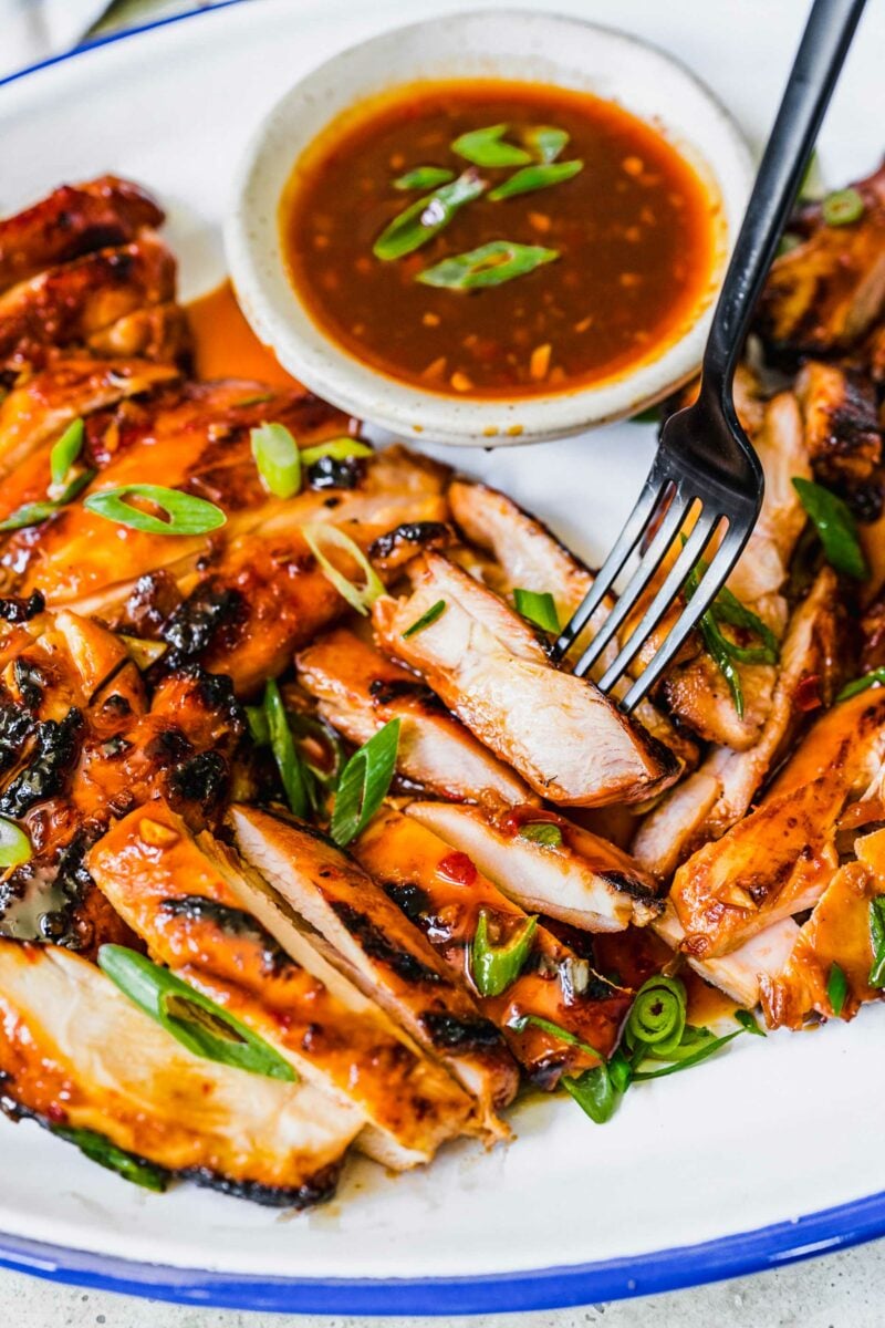 A fork is piercing a single slice of grilled chicken. 