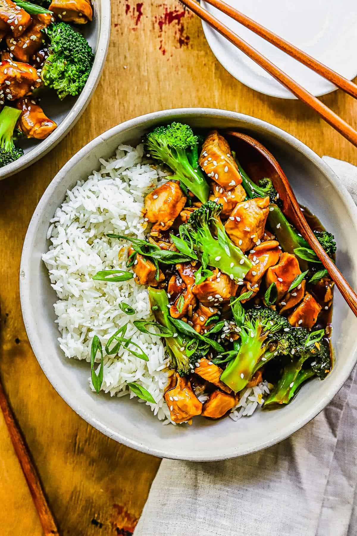 overhead shot of teriyaki chicken and broccoli in a white bowl with white rice and wooden spoon