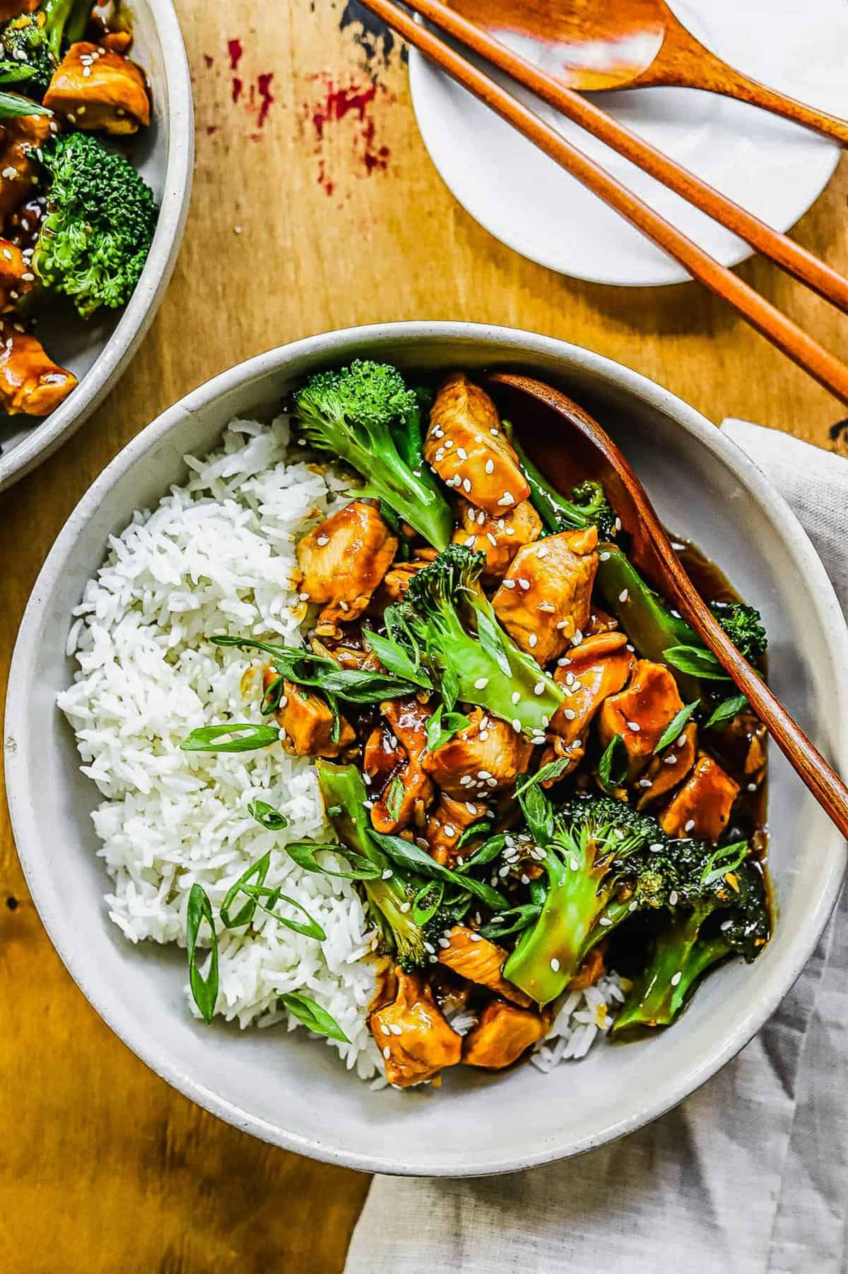 overhead shot of teriyaki chicken and broccoli in a white bowl with wooden spoon