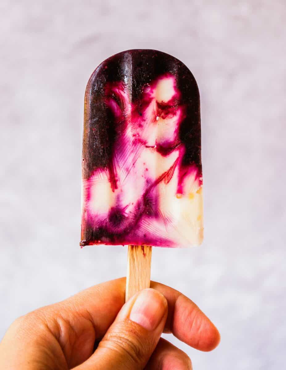 A popsicle is being held up by a hand in front of a white background. 