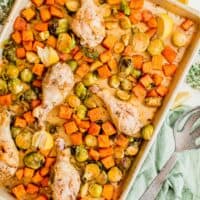 lemon pepper drumsticks and roasted vegetables on a rimmed metal sheet pan next to fresh lemon slices