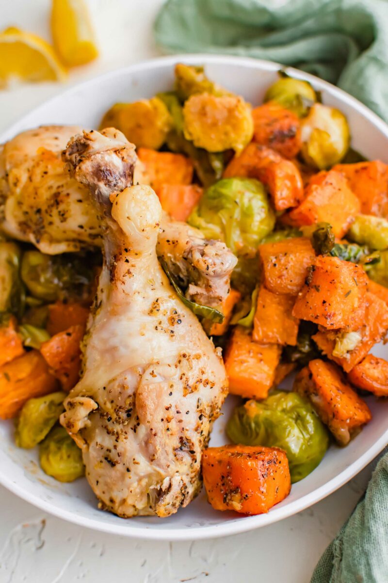 lemon pepper drumsticks on a white plate with roasted brussels sprouts and sweet potato cubes