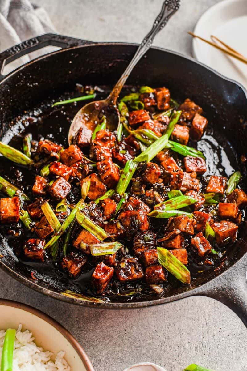 A spoon is placed in a pan filled with tofu and green onions. 