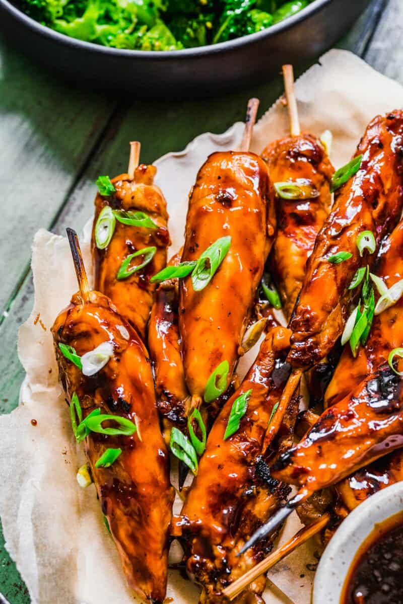 Scallions are chopped and garnish a pile of grilled chicken skewers. 