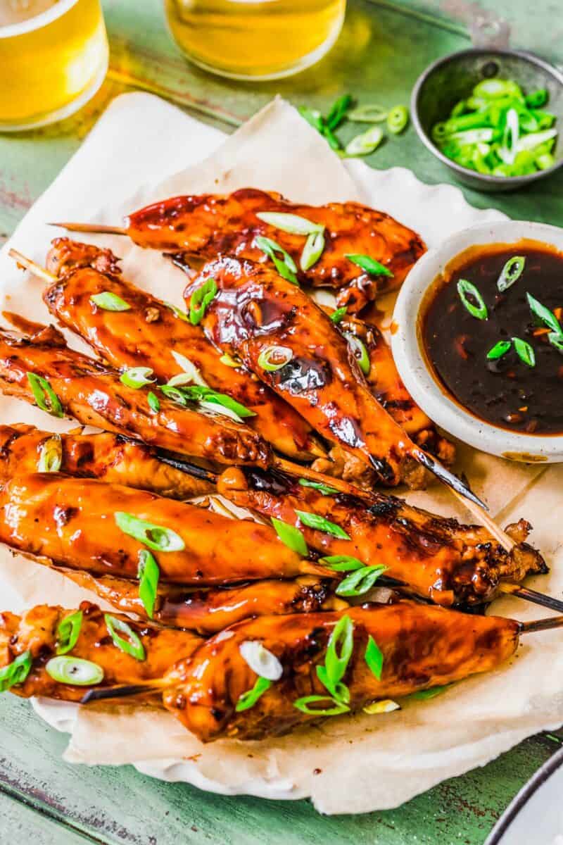 Garnished chicken skewers are placed next to a small bowl of teriyaki sauce.