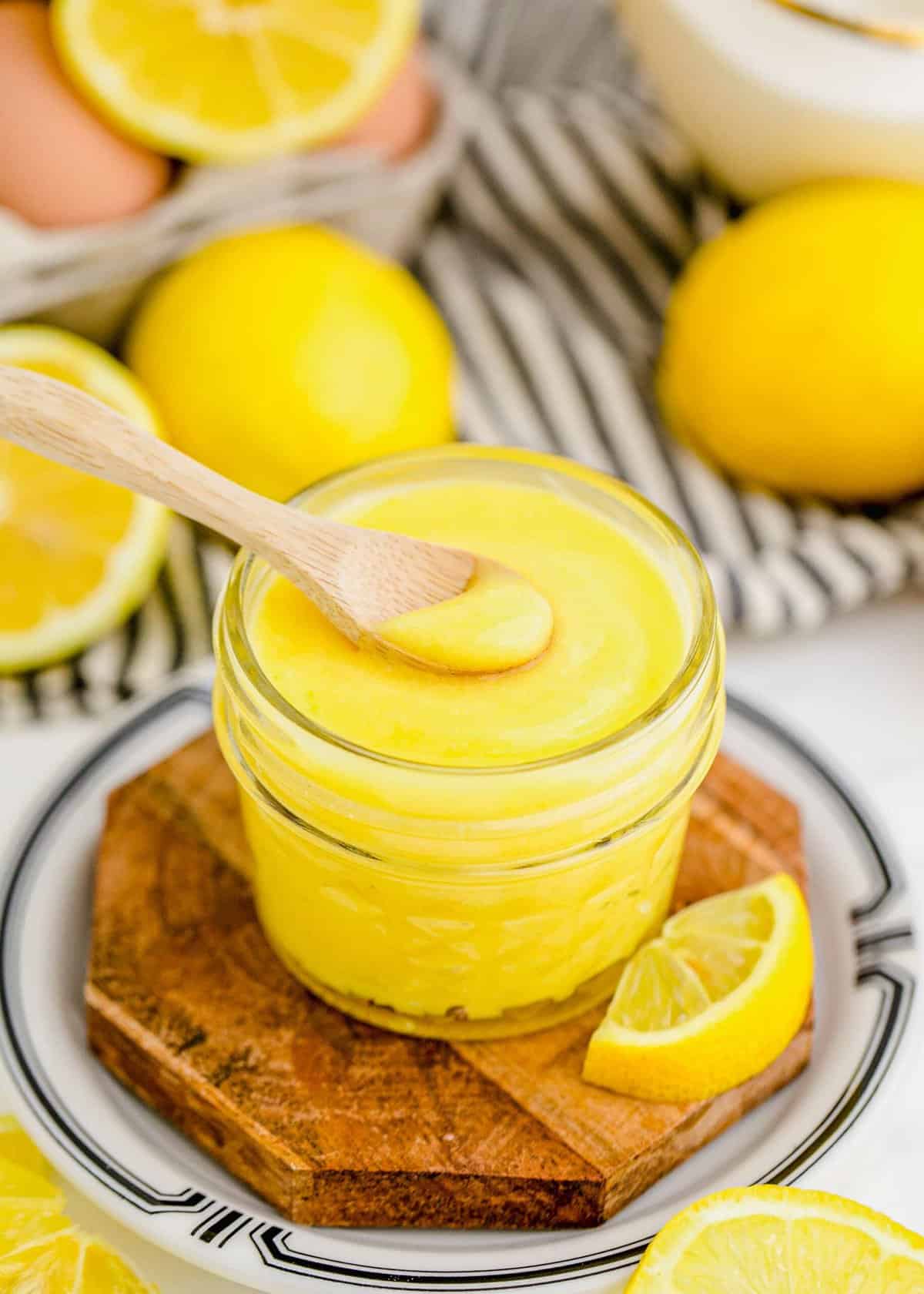 Jar of lemon curd with spoon, with fresh lemons in background