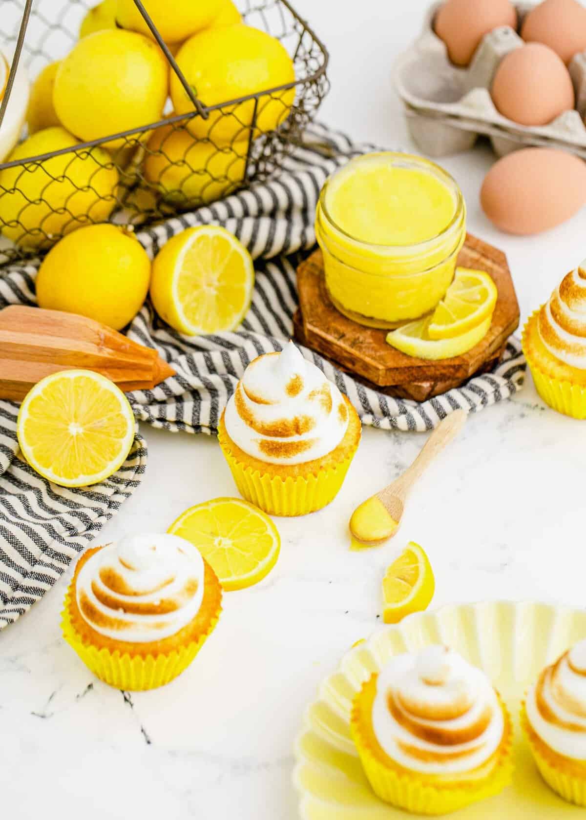 Lemon meringue cupcakes with lemon curd, lemons, and eggs in background