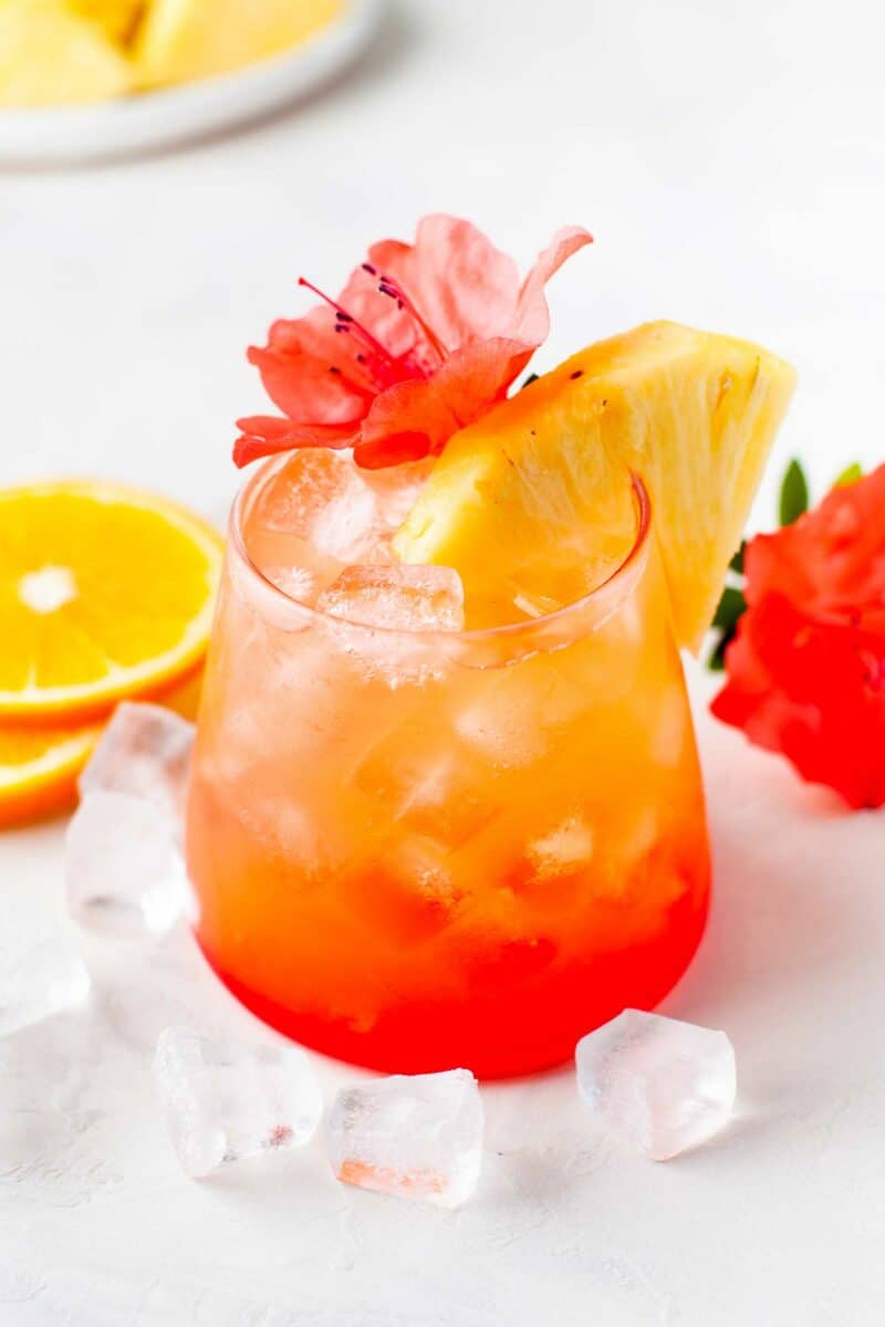 A glass of punch is placed on a table with ice cubes around it.