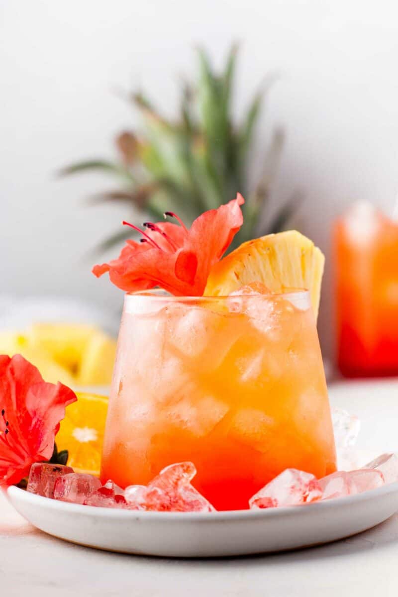 A glass of punch is garnished with a flower and a pineapple wedge. 