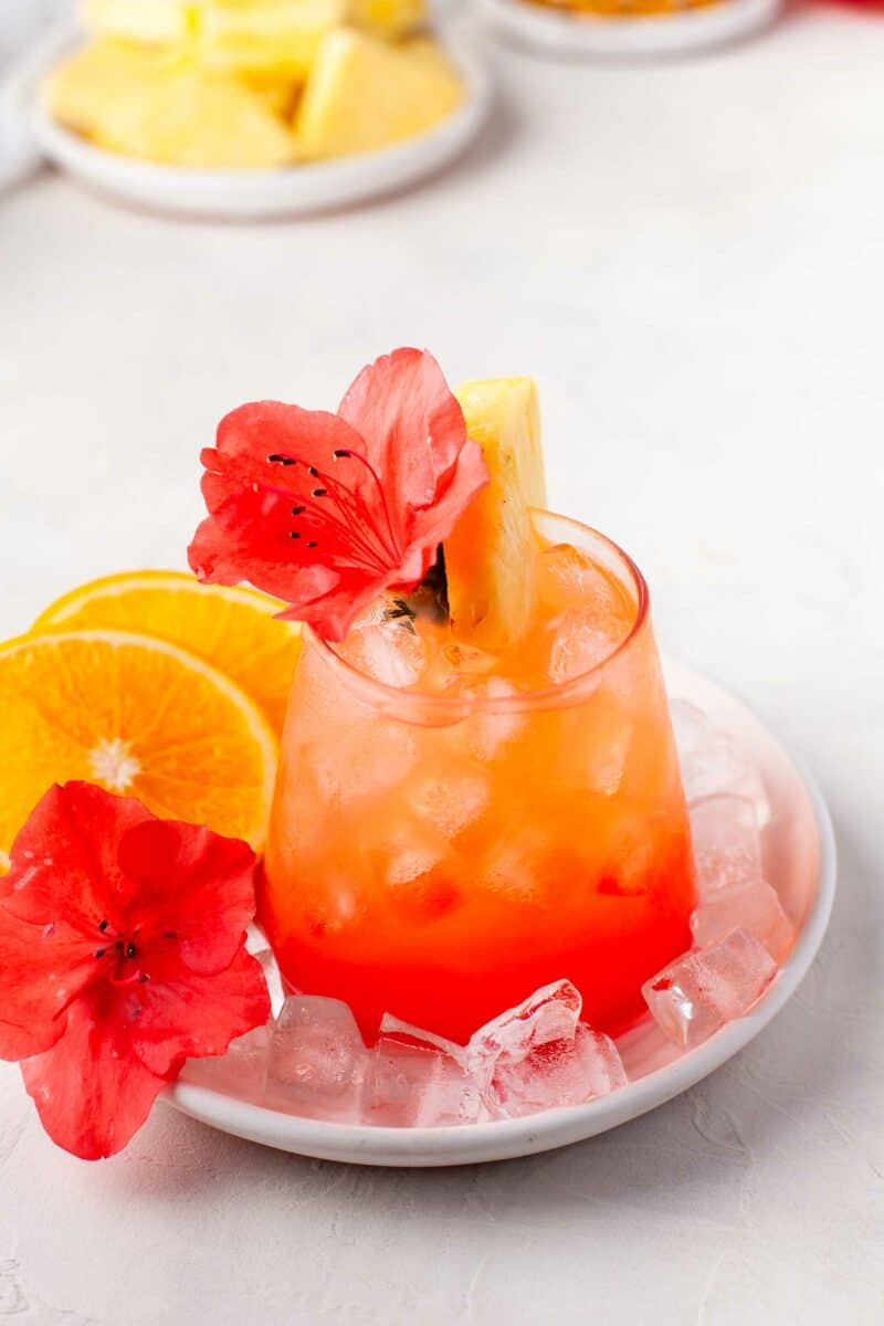 A glass of punch is presented on a round white plate with ice cubes. 