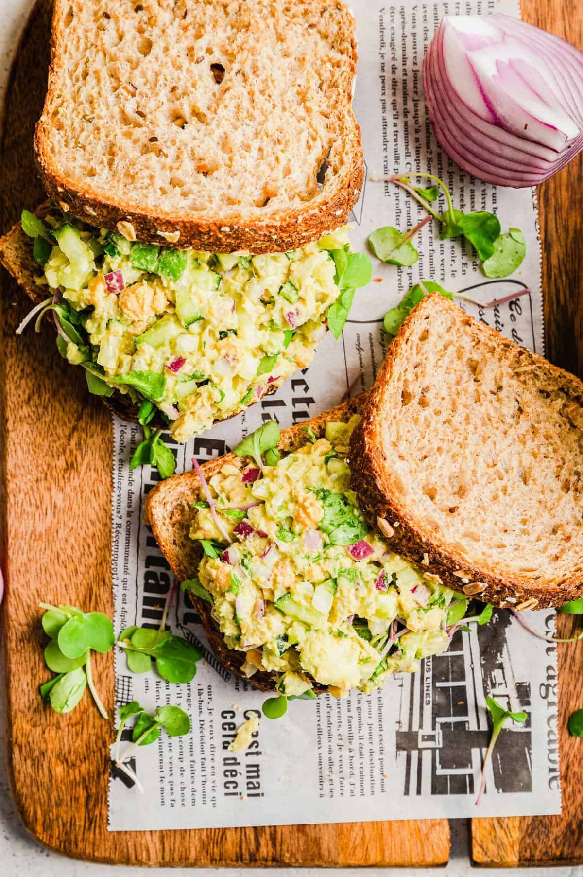 Two smashed chickpea sandwiches on board lined with newspaper