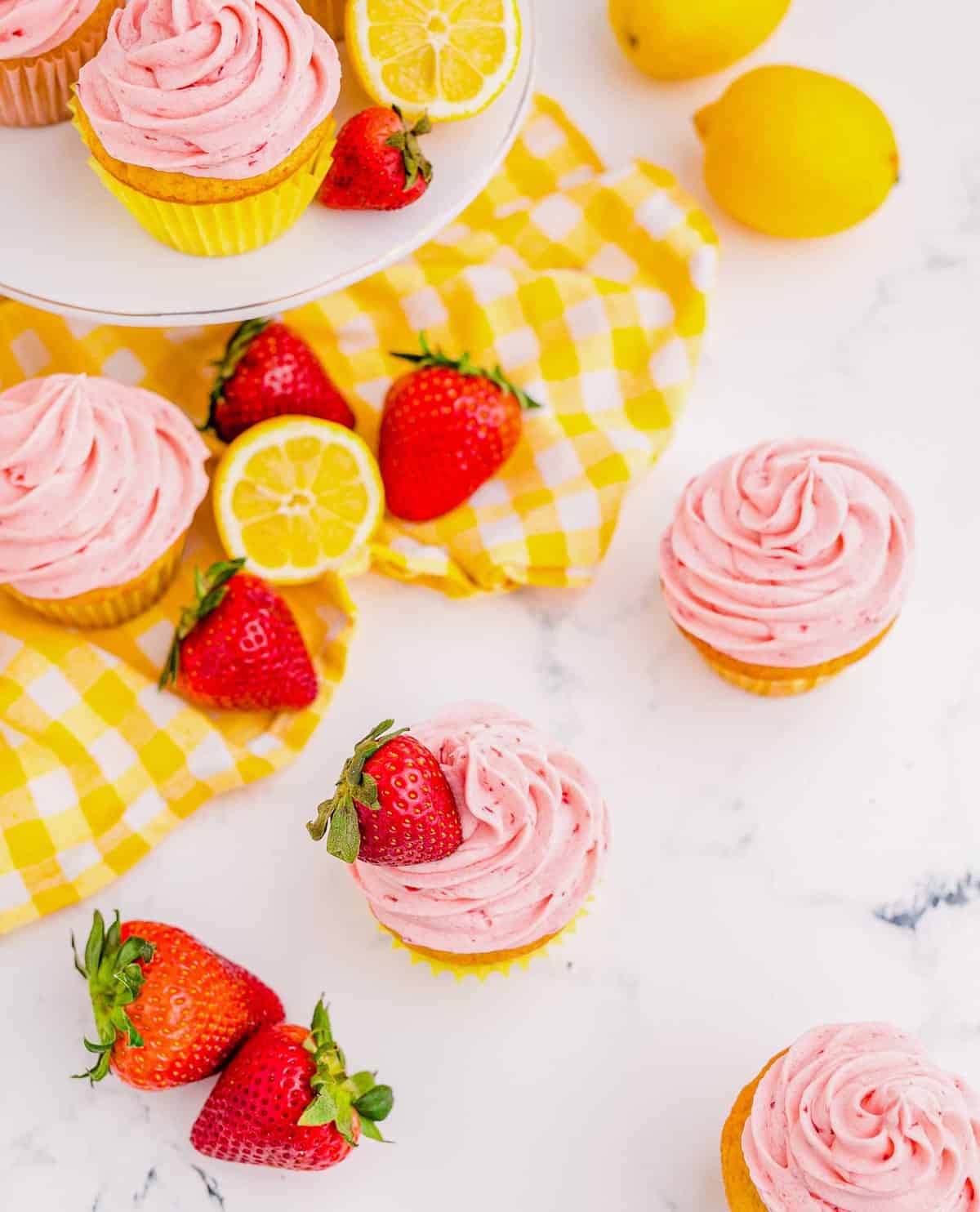 Strawberry lemonade cupcakes on counter and cake stand with lemons and strawberries