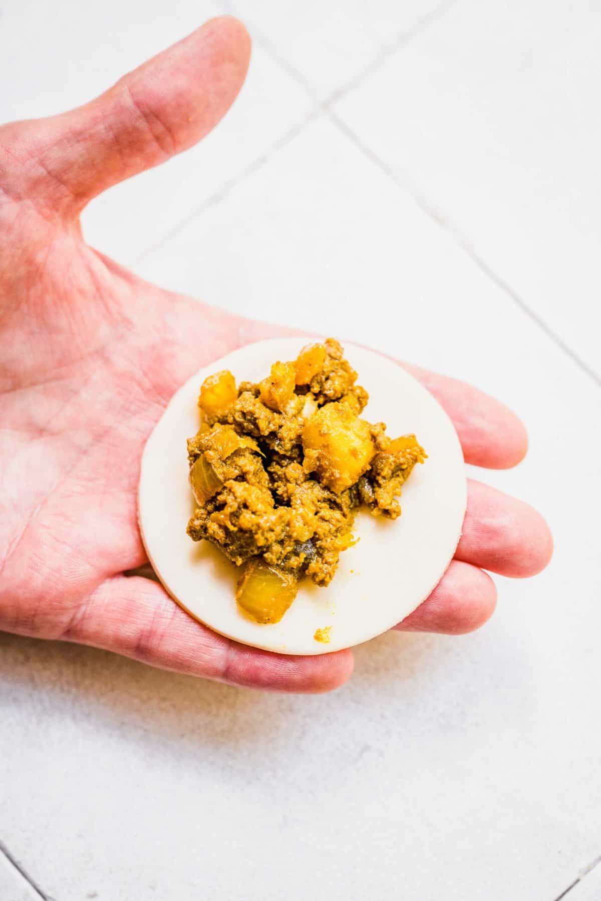 Hand holding circle of dough with beef curry filling on top