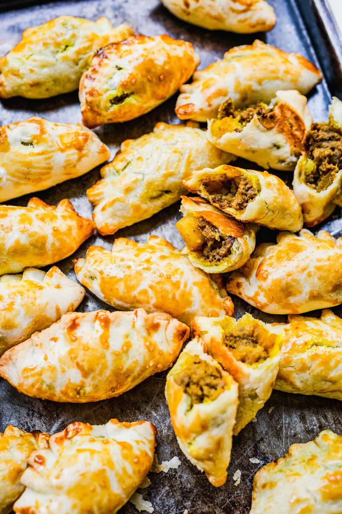 Chinese curry pockets on baking sheet, with some cut open to show filling
