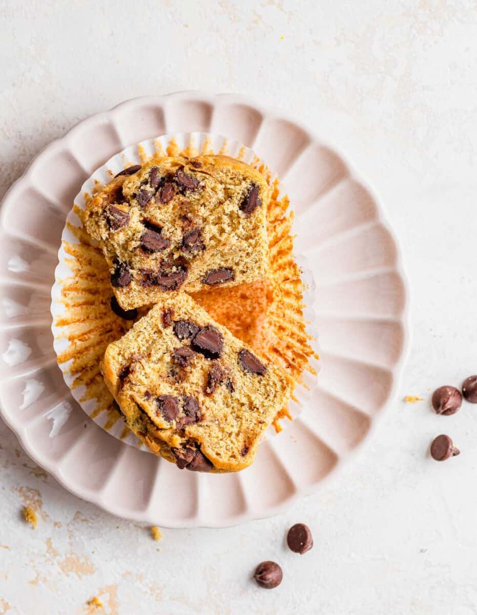 A muffin on a white plate has been cut in half to reveal a cooked center. 