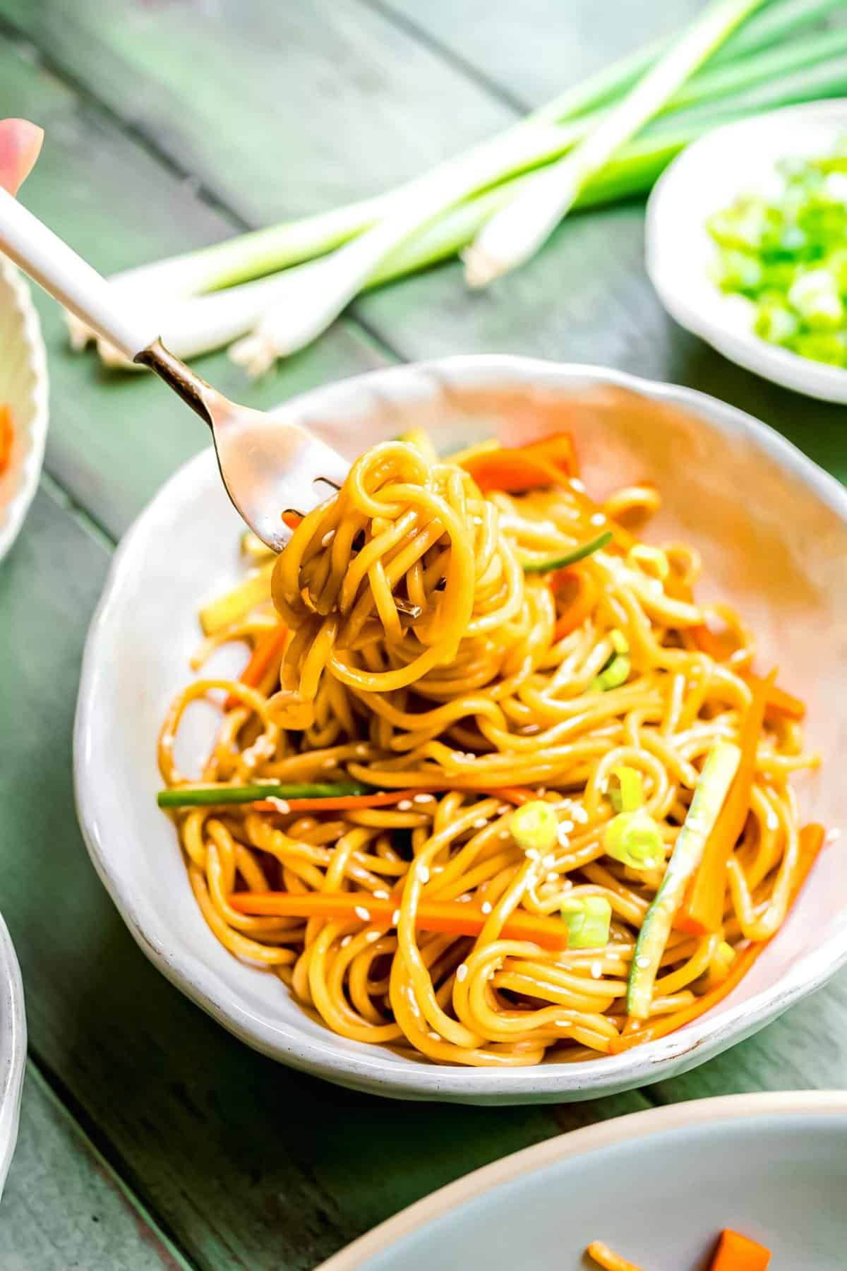 A fork lifting cold sesame noodles from a large white bowl.