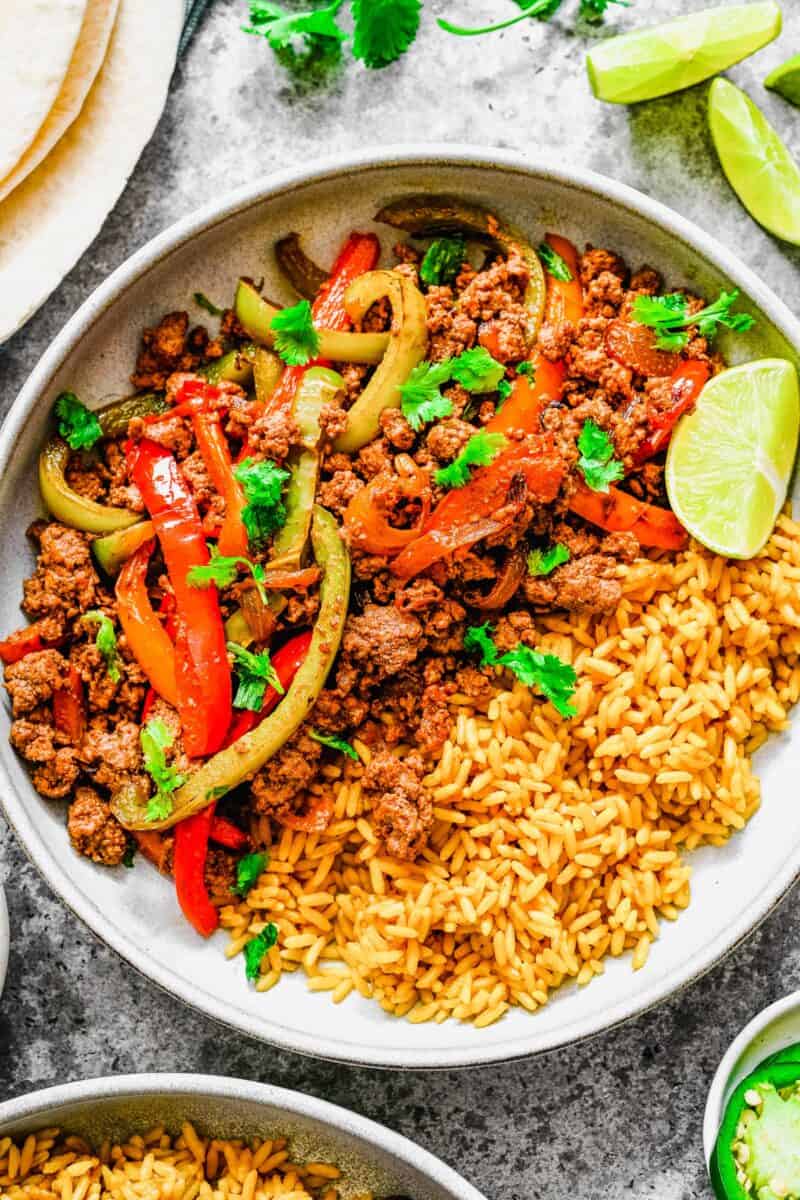 A white bowl is filled with rice, veggies, and ground beef. 
