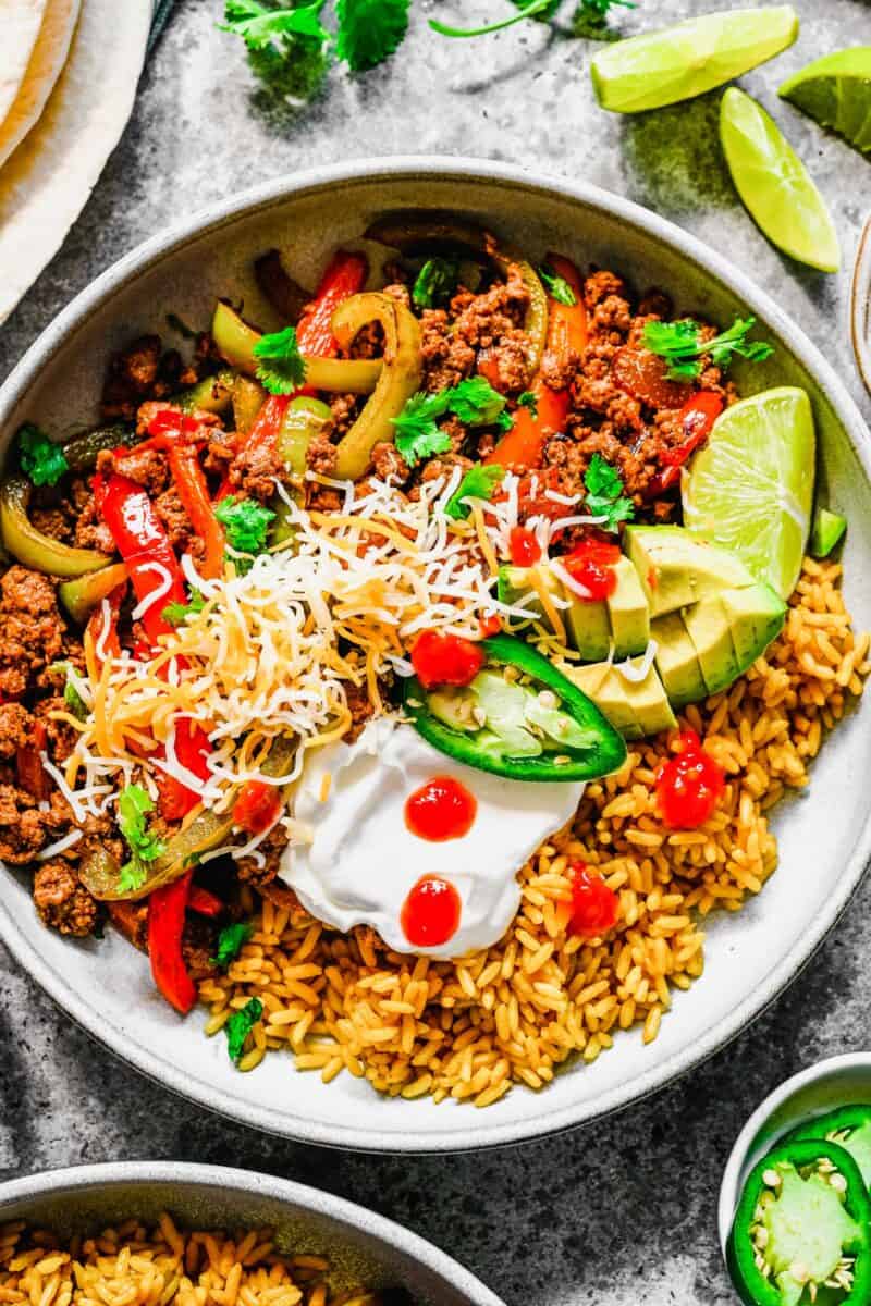 A fajita bowl is presented with a few drops of hot sauce and fresh jalapeno slices. 