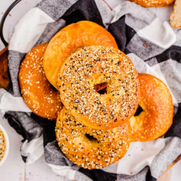 A pile of bagels are placed on a checkerboard tea cloth.