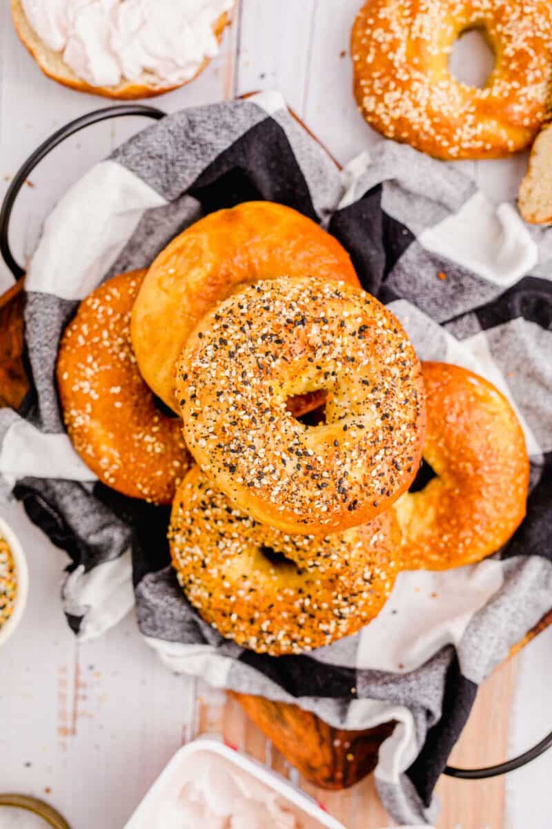 A pile of bagels are placed on a checkerboard tea cloth. 