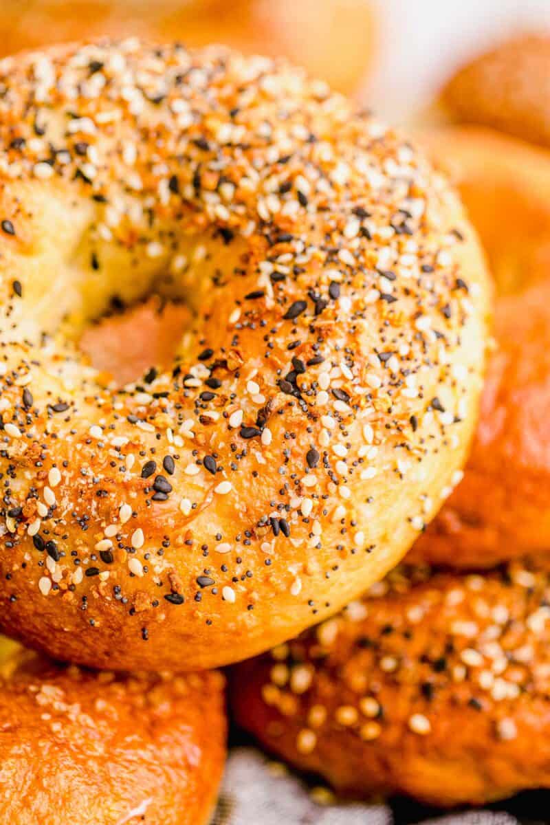 A sesame seed covered bagel is placed on top of other bagels. 
