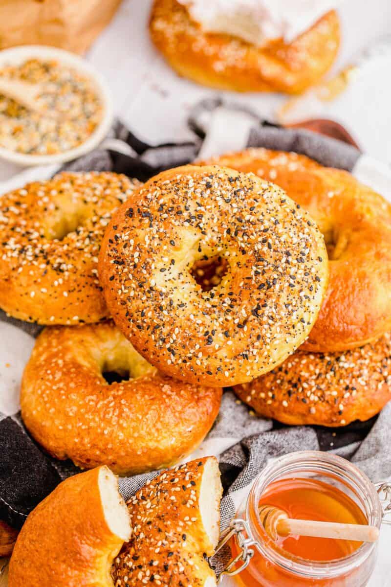 A pile of bagels is placed next to a glass jar of honey. 