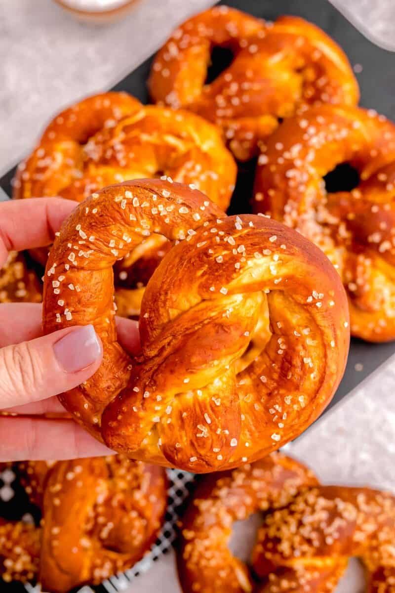 A hand is holding up a baked soft pretzel. 