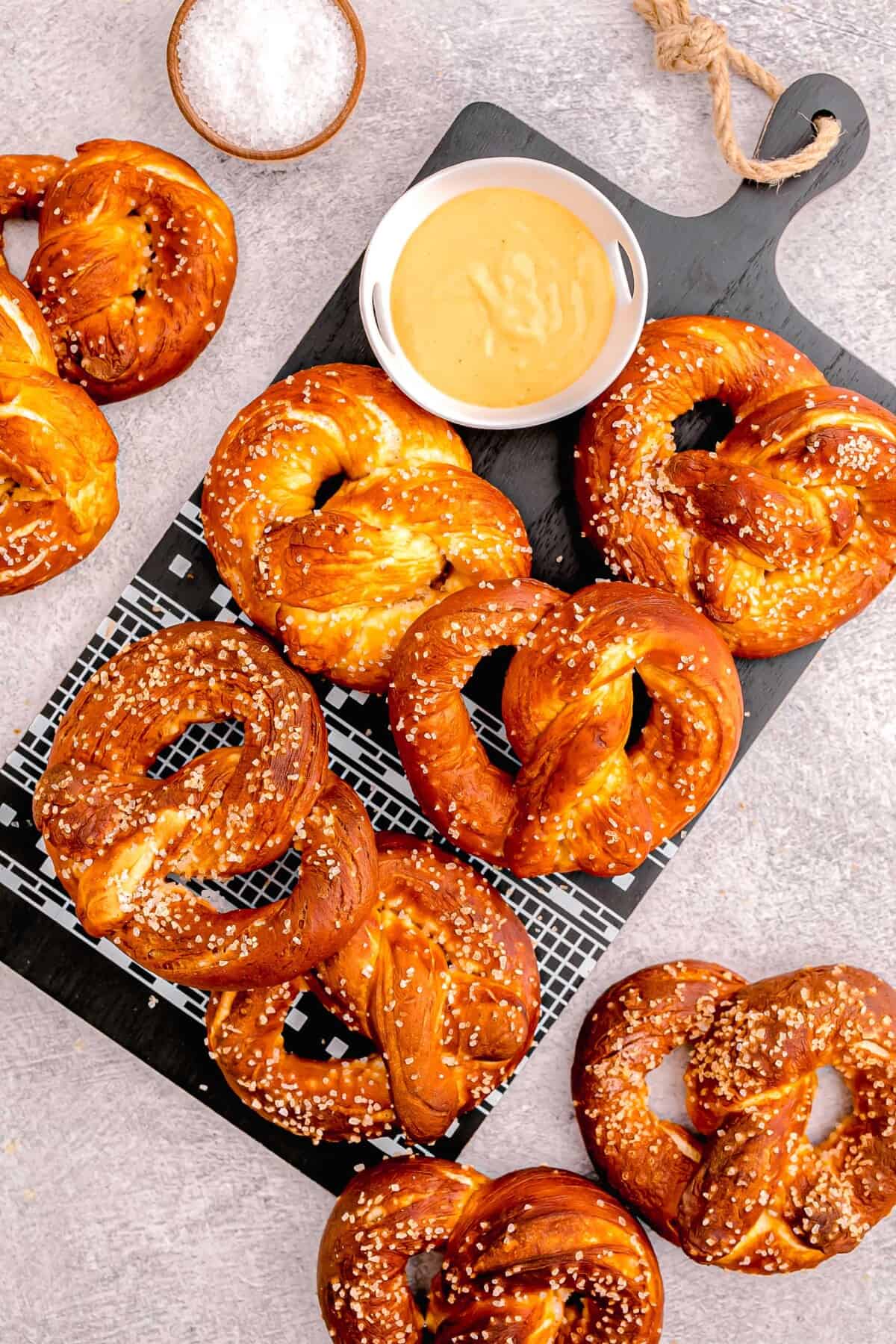 overhead image of homemade soft pretzels on black wooden cutting board next to beer cheese dip