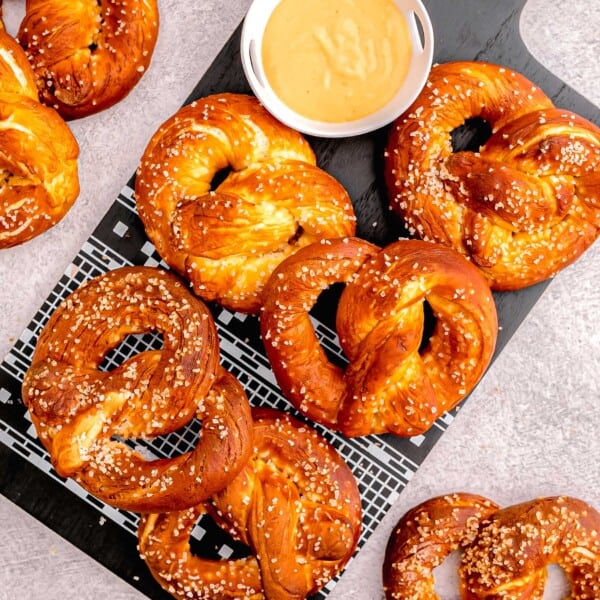 overhead image of homemade soft pretzels on black wooden cutting board next to beer cheese dip
