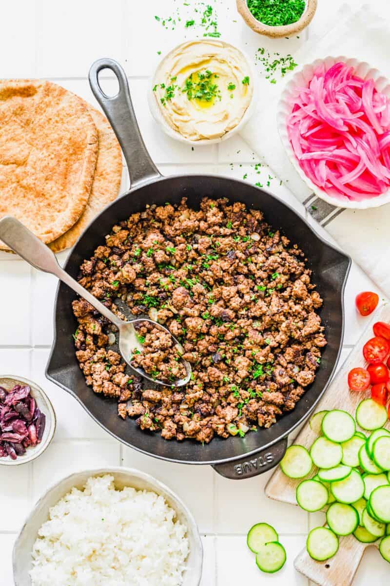 A spoon is placed in a large skillet filled with cooked ground beef. 