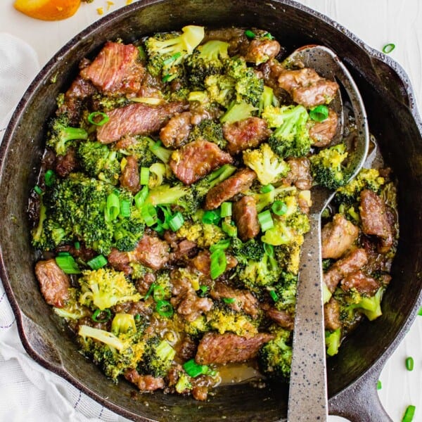 Overhead view of orange beef in a skillet with a metal serving spoon.