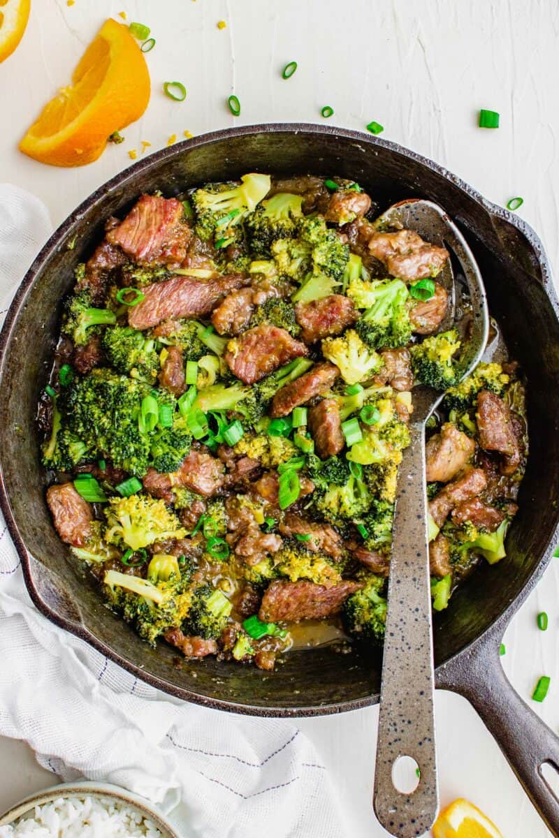 A large spoon is dipping into a pot filled with cooked broccoli and beef.
