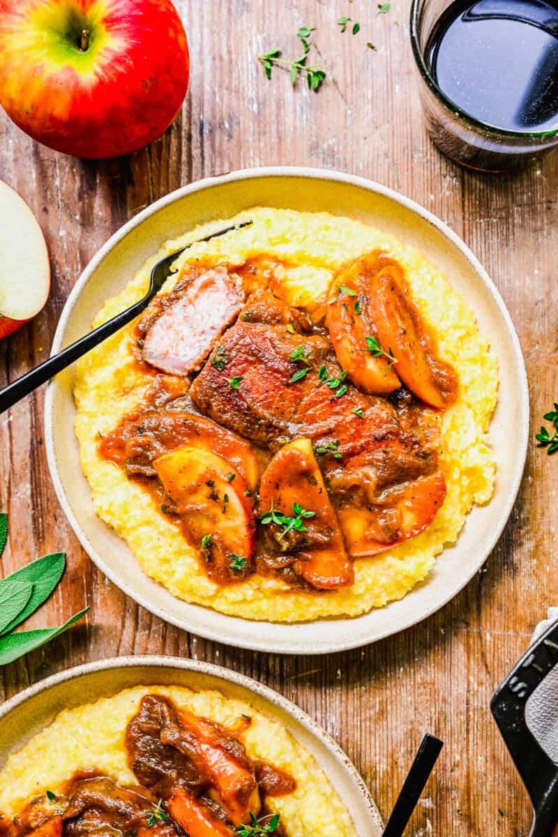 Apple butter pork chops are presented on top of cooked polenta on a white plate. 