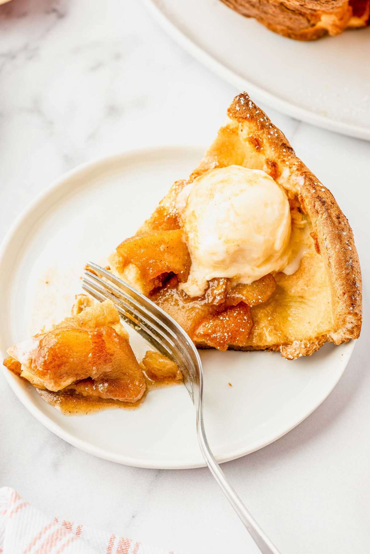 A fork cuts through a single slice of Apple Cinnamon Dutch Baby on a plate.