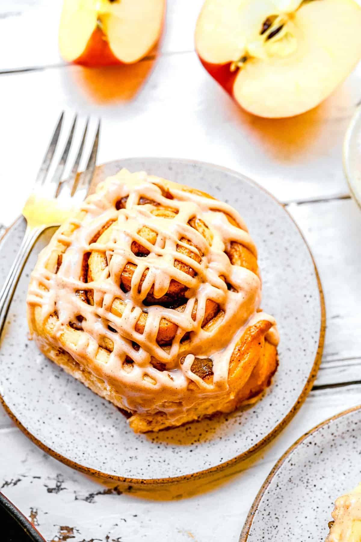 One apple pie cinnamon rolls on a gold rimmed dessert plate with a fork.
