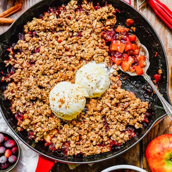 A pan of apple cranberry crisp with a silver serving spoon sitting atop.