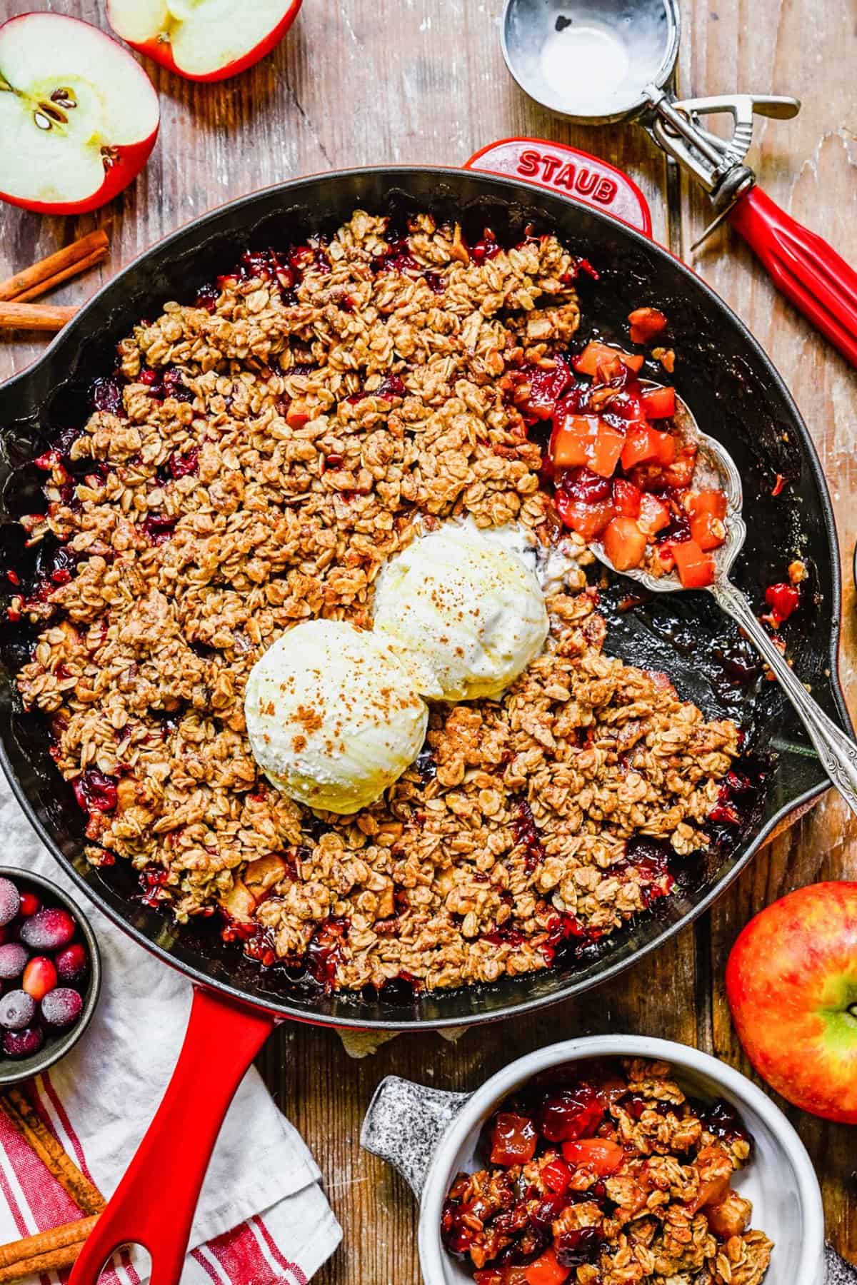 A pan of apple cranberry crisp with a silver serving spoon sitting atop.