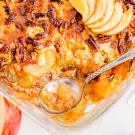 A pan of golden brown Caramel Apple Dump Cake topped with toasted pecans is served from pan. A portion sits next to the pan topped a la mode with vanilla ice cream and caramel sauce.