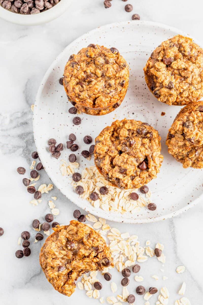 Cookie cups are placed on a white surface with chocolate chips and oats. 