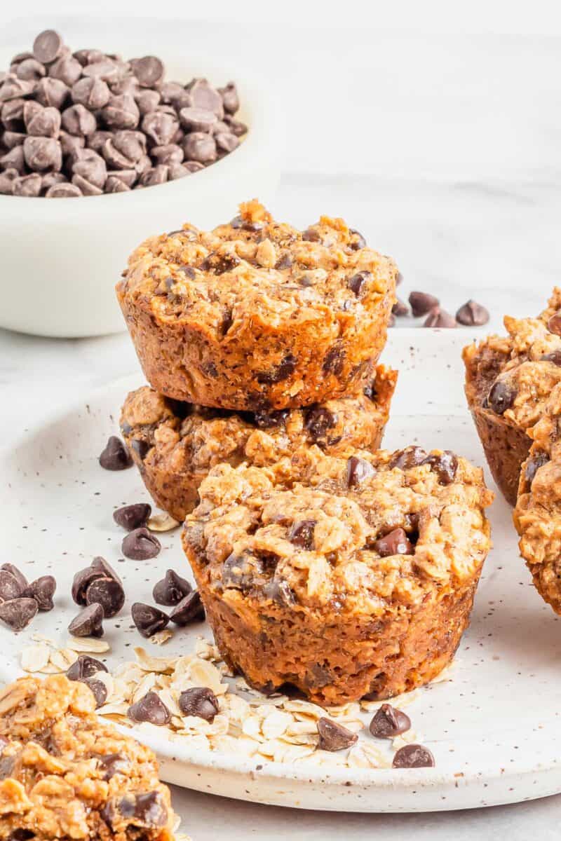 Several cookie cups are stacked on a white plate next to chocolate chips and oats. 